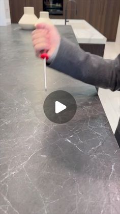 a person holding a red object on top of a marble countertop in a kitchen