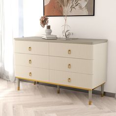 a white dresser with gold handles and two green candles sitting on it's top