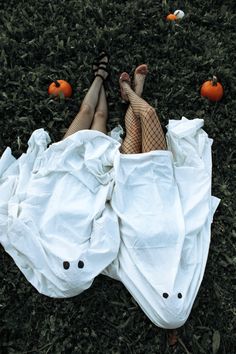 a person laying on top of a white sheet covered in plastic bags and pumpkins