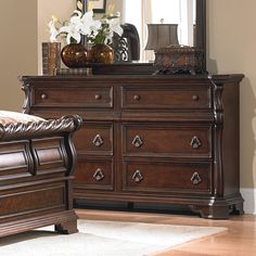 a bedroom scene with focus on the dresser and bed, which has a large mirror above it