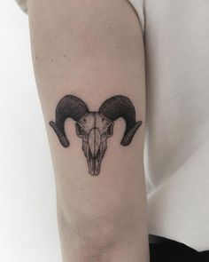 a ram skull tattoo on the left arm with horns in black and grey ink,