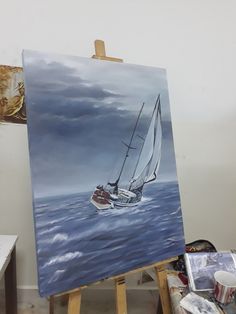 a painting of a sailboat in the ocean on an easel with paintbrushes