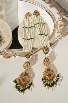 The "Sanjana - Long Saharay Earrings and Maang Tikka set" is an embodiment of imperial classics and a celebration of the richness of Navratan stones. This exquisite set is curated to evoke the essence of grandeur and festivity. The set includes a dazzling maang tikka and a pair of brilliant earrings, each adorned with breathtaking stonework and pearl moti, reflecting sheer class. The earrings feature saharay and a Navratan motif at the tip, creating an alluring visual spectacle. With an approxim Temple Jewelry Style Tikka For Eid Celebration, Temple Jewelry Tikka For Eid Celebration, Eid Celebration Temple Jewelry Tikka, Temple Jewelry Bridal Earrings For Eid Celebration, Traditional Style Danglers With Tilla For Eid, Traditional Danglers With Tilla For Eid, Temple Jewelry Bridal Earrings For Eid, Temple Jewelry Bridal Earrings For Festive Eid, Bridal Tilla Earrings For Festive Celebrations