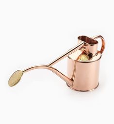 a metal teapot with a gold spoon in the shape of a watering can on a white background