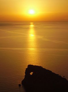 the sun is setting over an ocean with rocks