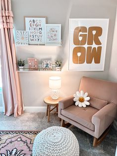 a chair and ottoman in a small room with pink curtains, pictures on the wall