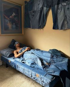 a man laying on top of a bed covered in blue jean pants next to a painting