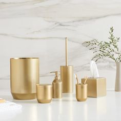 gold bathroom accessories set on marble countertop next to white vase with greenery in it