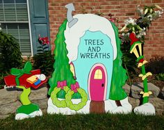 there is a sign that says trees and wreaths in front of a house with plants