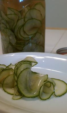 sliced cucumbers on a white plate next to a jar