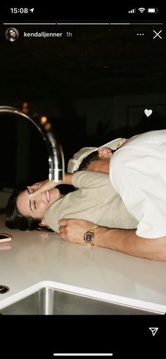 a woman laying on top of a kitchen counter next to a faucet and sink