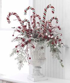 a vase filled with candy canes on top of a white table next to a window