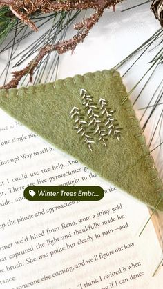 an ornament made out of felt sitting on top of a book next to pine needles