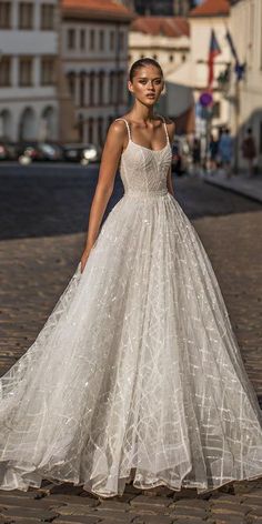 a woman in a white wedding dress standing on a brick road with buildings behind her