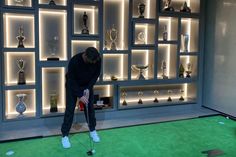 a man playing golf in front of a display case with trophies on the wall behind him