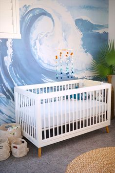 a white crib in front of a blue wave painted on the wall behind it