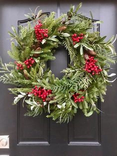 a christmas wreath hanging on the front door with holly and red berries, pine cones and evergreen leaves