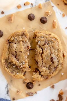 two chocolate chip cookies on top of parchment paper with one cookie cut in half and the other half eaten