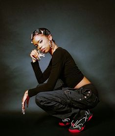 a woman sitting on the ground with her hand under her chin and wearing red shoes