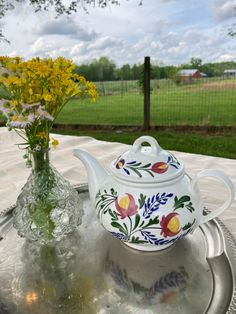 a tea pot and vase with yellow flowers on a silver tray in front of a fence