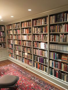 a room filled with lots of books on top of a book shelf next to a rug