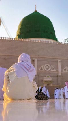 a person sitting on the ground in front of a building with a green domed roof