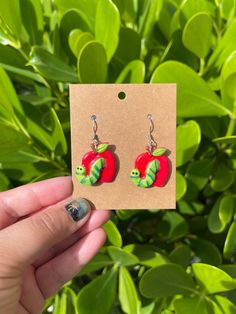 a pair of red apple shaped earrings with green leaves in the background and a brown card attached to it