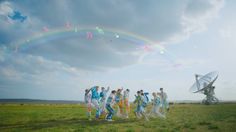 a group of people standing on top of a lush green field under a rainbow filled sky