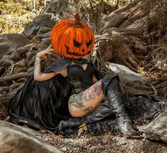 a woman in a black dress with a pumpkin on her head sitting on the ground