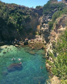 people are swimming in the clear blue water near some cliffs and trees on top of them