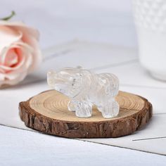 a clear glass elephant figurine sitting on top of a wooden stand next to a pink rose