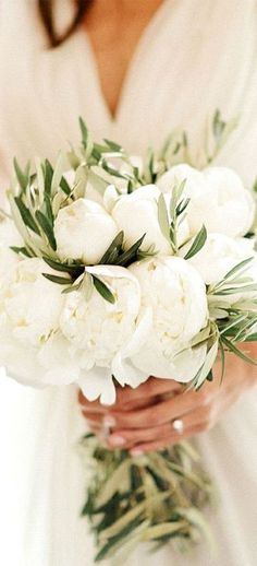 a bride holding a bouquet of white peonies and greenery on her wedding day