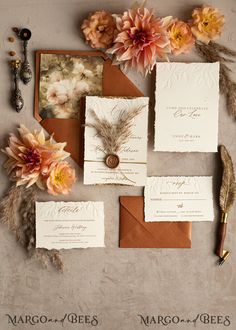 the wedding stationery is laid out with flowers and feathers