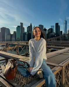 a woman sitting on top of a metal bench in front of a cityscape