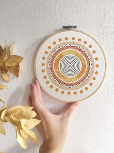 a hand is holding up a cross - stitch pattern on a white wall next to some leaves