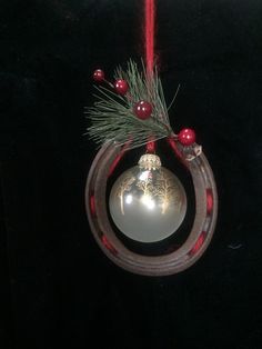 a christmas ornament hanging from a red ribbon on a black background with pine branches