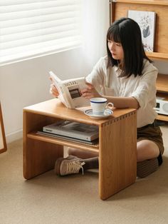 a woman sitting on the floor reading a book and holding a coffee cup in front of her