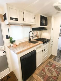 a kitchen with white cabinets, black appliances and a rug on the floor in front of it