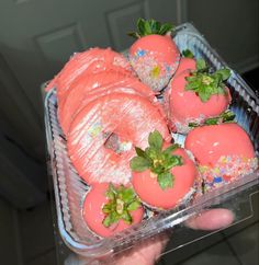 a plastic container filled with pink donuts covered in frosting and sprinkles