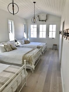 three beds in a room with white walls and wood floors, along with two lamps hanging from the ceiling