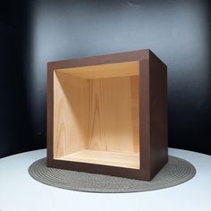 an empty wooden box sitting on top of a white round table with a black wall in the background