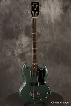 an electric bass guitar sitting on top of a black stand in front of a gray background