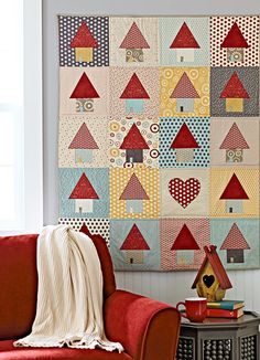 a red couch sitting next to a wall with a quilt on it's side