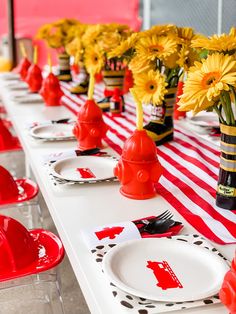 the table is set with red and white plates, yellow flowers, and fire hydrant vases