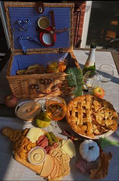 an assortment of food and drinks on a table with a picnic basket in the background