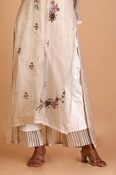 Ivory tunic in jute silk base with floral thread embroidery and kalis in the back. Comes with an inner. - Aza Fashions Off White Floral Embroidered Kurta For Spring, Spring Off White Sets With Embroidered Border, Festive Linen Kurta With Embroidered Border, Off White Embroidered Kurta For Spring, Spring Cream Kurta With Dupatta, Cream Kurta With Dupatta For Spring, Festive White Sets With Embroidered Hem, Floral Embroidered Tunic Kurta For Wedding, Cream Kurta With Floral Embroidery For Spring