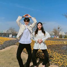 two people standing next to each other in front of yellow flowers and blue sky with buildings in the background