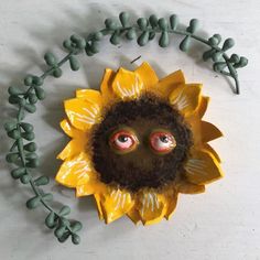 a paper sunflower with eyes and leaves on the top is surrounded by green beads