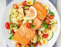 a white plate topped with salmon, pasta and veggies on top of a table