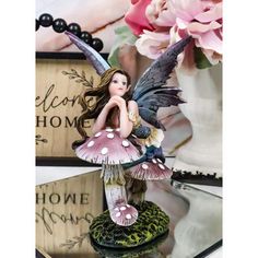 a fairy figurine sitting on top of a table next to pink flowers and a vase